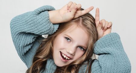 Portrait of positive happy child with curly hair, holding index fingers above head, mimicking horns and smilingの写真素材