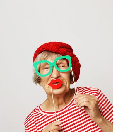 lifestyle, people and party concept: funny grandmother wearing red clothes holding falce glassesの写真素材