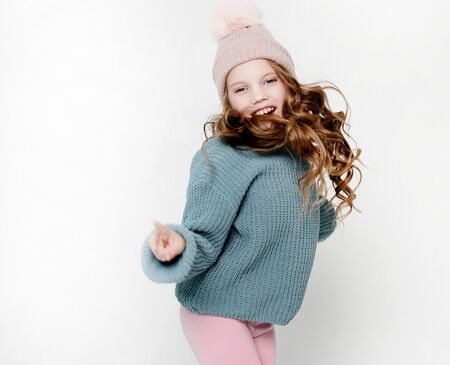 Childhood, fashion and people concept: Little girl in pink hat and blue sweater jumping on the white background.の写真素材