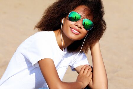 Charming amazing afro american young woman in sunglasses listening to music in headphones on her...