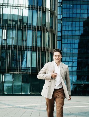 Young happy man in a business suit poses near a modern business center on a summer dayの写真素材