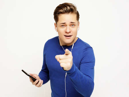 young handsome man on white studio background listening to music on earphones