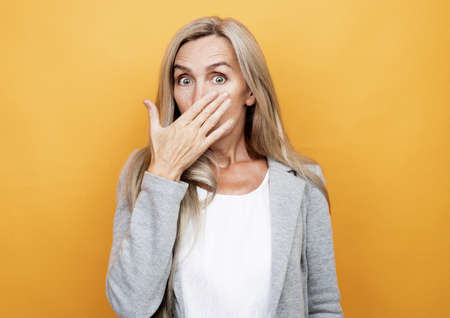 lifestyle, emotion and people concept: senior surprised woman. Isolated over yellow background.