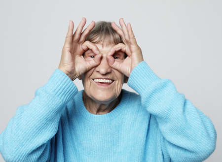 An elderly woman makes glasses from her fingers, amuses herself and poses. A fun time at any age.の写真素材