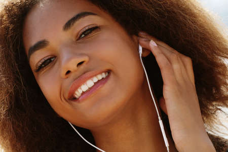 Young african american girl using mobile phone and headphones, smiling, close upの写真素材