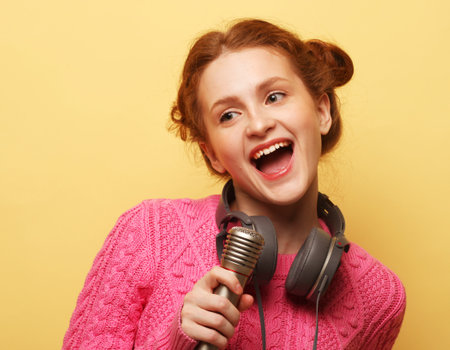Beauty redhair woman wearing casual with microphone over yellow background.の写真素材