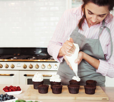 Young Woman making creamy top of cupcakes closeup.の写真素材