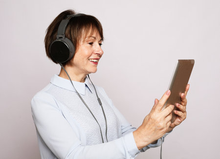Elderly woman in headphones with tablet over grey backgroundの写真素材