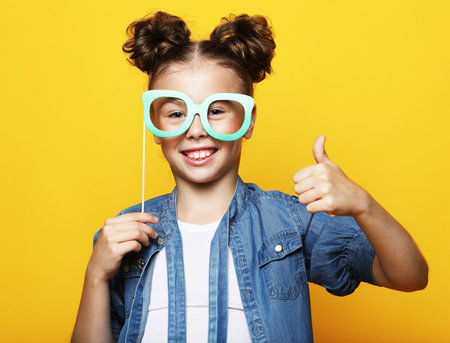 party, childhood and people concept: little girl with a paper accessories over yellow background.の写真素材