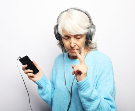 Senior beautiful woman in blue sweater listening music with a headphones. Over white background.の写真素材