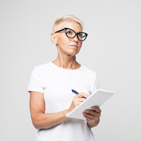 Photo portrait of senior female teacher writing notes in organizer wearing eyeglasses isolated on...