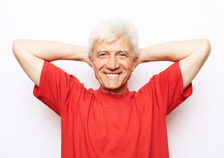Handsome senior man wearing red t-shirt relaxing and stretching with arms and hands behind head and neck, smiling happy. Over white background.の写真素材