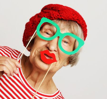 lifestyle, people and party concept: funny grandmother wearing red clothes holding falce glasses and ready for partyの写真素材