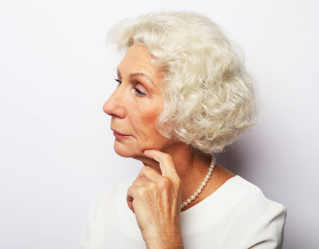 Emotion, lifestyle and old people concept: Thoughtful senior lady with her fingers to her chin reminiscing and recalling fond memories, close up portrait over white backgroundの写真素材