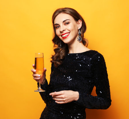 Young stylish woman drinking champagne, celebrating new year, wearing evening dress.の写真素材