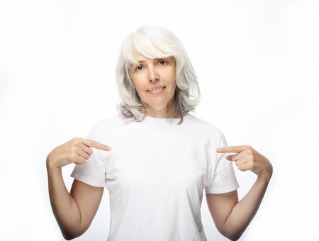 Lifestyle, emotion and old people concept: Senior beautiful gray-haired woman wearing casual t-shirt over isolated white background looking confident with smile on face, pointing oneself with fingers proud and happy.の写真素材