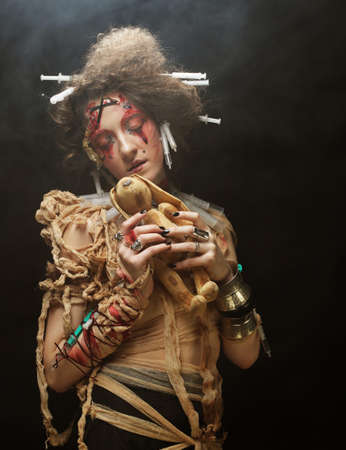 Young blond woman with creative make up and hairstyle holding little rabbit. Halloween theme.