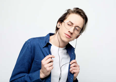 Happy young stylish man wearing casual and eyeglasses adjusting his headphones and smiling while...