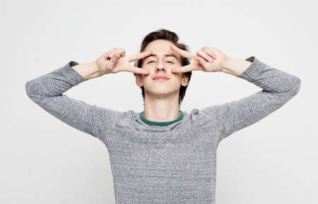 young man posing in white isolated studio background and showing the victory sign, looking at the camera, casual styleの写真素材