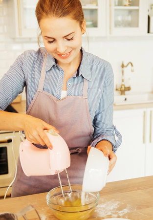 Young woman baking a cake in the kitchen standing at the counter in her apronの写真素材