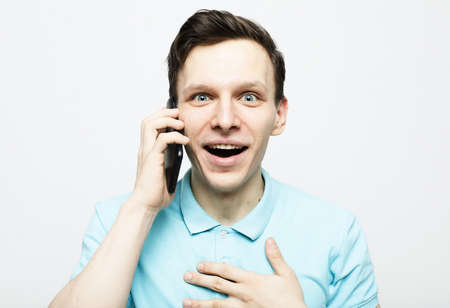 Happy young man in blue shirt gesturing and smiling while talking on the mobile phoneの写真素材