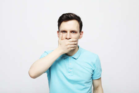 Lifestyle, emotion and people concept: A young man dressed in a plaid blue shirt covers his mouth with his palms.の写真素材