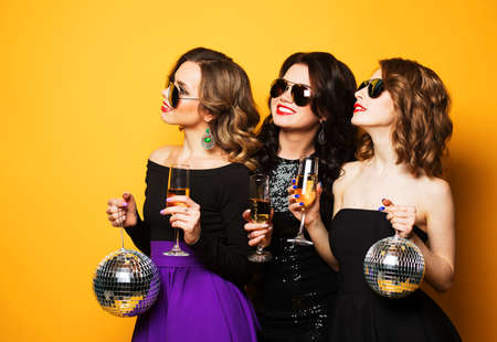Three joyful charming young women friends with disco balls drinking champagne