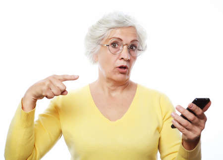 Exciting news. An elderly woman has heard the news and points to the phone with her finger, drawing attention. Photo over white background.の写真素材
