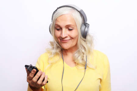 Enjoy every day. An elderly woman smiles and listens to music while wearing headphones over white background.の写真素材
