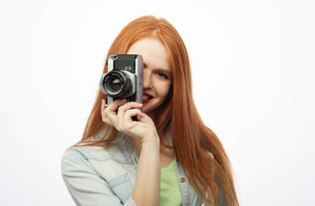 Amazed young pretty redhair woman holding a vintage camera over white background.の写真素材