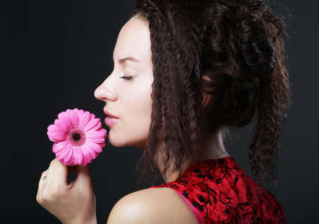 Young beautiful woman wearing red dress holding pink gerber flowerの写真素材