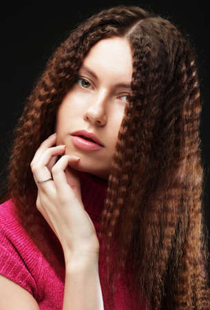 Beautiful girl with long wavy hair. Brunette with curly hairstyle. Close up picture over dark...