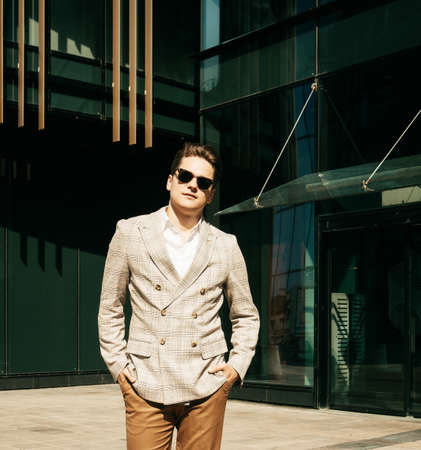 Business, success and people concept: Portrait of a young businessman in sunglasses, close-up, a man stands next to a modern officeの写真素材