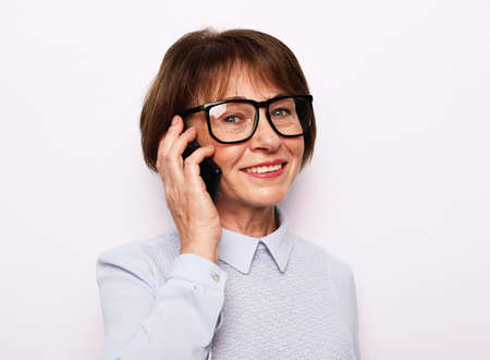Modern Communication. Happy senior woman in eyeglasses using mobile phone over white background....