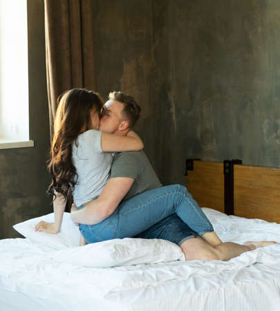 Young couple playfully hugs on the bed, casual wear, cozy interior.の写真素材