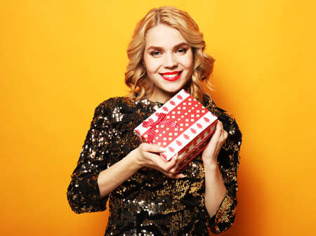 Portrait of a happy smiling woman in dress holding present box isolated over yellow background