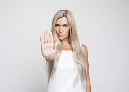 Senior grey-haired woman doing stop sign with serious and confident expression over grey background