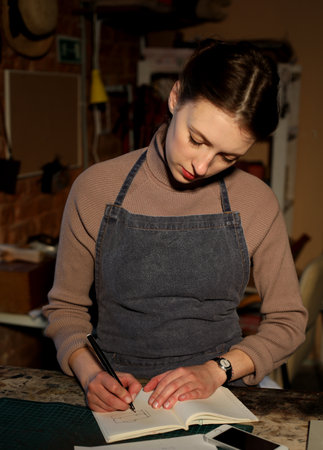 Lifestyle, freelance and home business concept: young brunette woman writes to notebook in sewing...