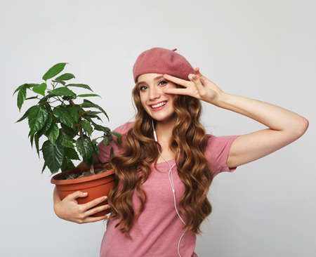 Smiling woman with long wavy hair wearing pink clothes, standing over grey background and holding flower in potの写真素材