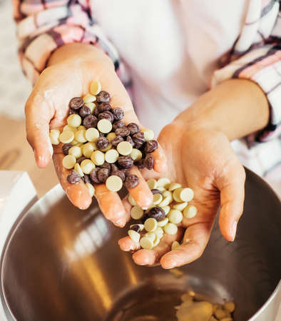 Close-up female hands holding chocolate drops - white and brown, for making chocolate ganache