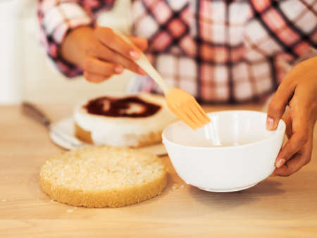Close-up female hands smearing cake cakes with creamの写真素材