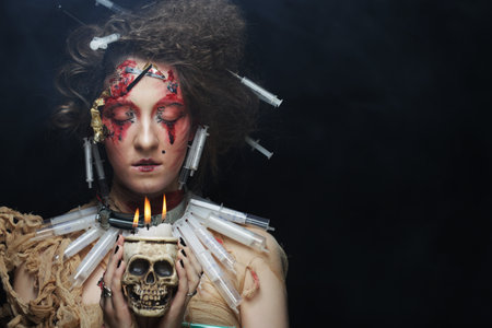 Young woman with creative makeup and hairstyle holding a candle in a skull candlestickの写真素材