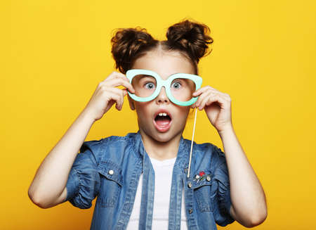 Party, childhood and people concept: little girl with a paper carnival accessories over yellow background.の写真素材