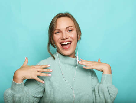 Cheerful young woman in blue sweater posing isolated on blue wall background studio portait. People lifestyle concept. Listen music with headphones and dancing.の写真素材