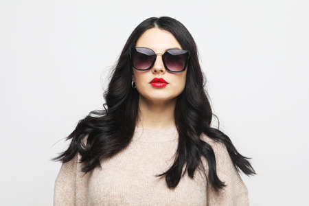Young woman wearing pink sweater and sunglasses, posing over gray backgroundの写真素材
