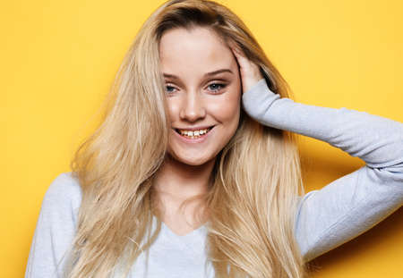 Pretty young blond woman wearing casual with cute smile poses alone against yellow background.の写真素材