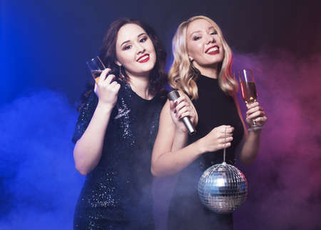 Two young women holding a glass of wine and disco ball at night clubの写真素材