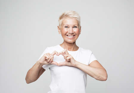 Perfect, nice, aged, old, pretty woman with short hair in t-shirt making, showing heart figure with fingersの写真素材