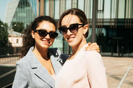 Closeup portrait, two office workers wearing sunglasses standing together outdors near modern business building.の写真素材