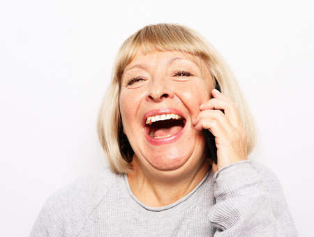 Pretty senior female in casual outfit using modern smartphone and laughingの写真素材